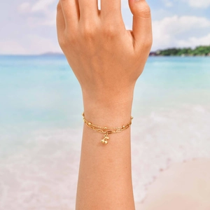 Gros plan d'un bracelet doré double couche avec pendentif cerise sur un fond de plage