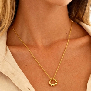 Gros plan sur un collier doré avec pendentif cercle noué porté par un mannequin élégant