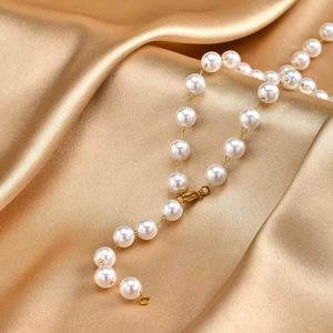 Close-up of pearl necklace with gold lobster clasp on silk background