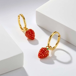 Detail of gold-plated hoop earrings with red strawberry charms on white geometric blocks