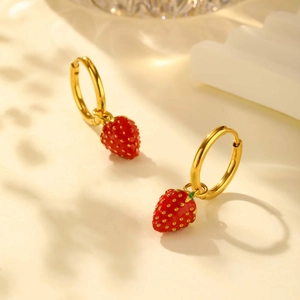 Detail of gold hoops with realistic red enamel strawberry charms on a clean background