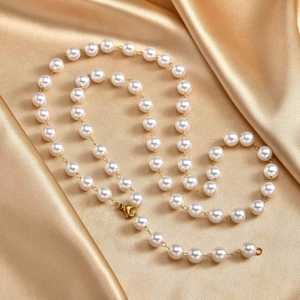 Detail of elegant gold Y-shaped necklace with white pearls on a golden silk fabric background