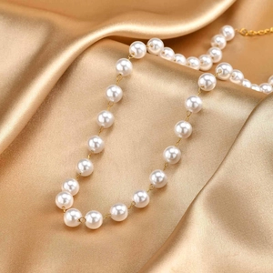 Detailed close-up of golden pearl Y-necklace on premium smooth silk fabric background