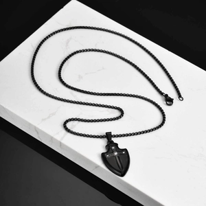 Détail macro du pendentif bouclier noir avec croix en relief et zircone sur marbre