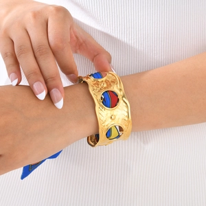 Detail of a gold wide cuff bracelet with a colorful silk scarf and hammered texture