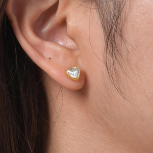 Close-up of heart-shaped gold-plated stud earring with white zircon on ear