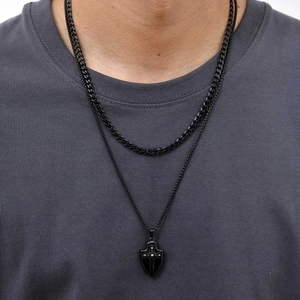 Gros plan d'une double chaîne gourmette noire avec pendentif bouclier à croix pour homme