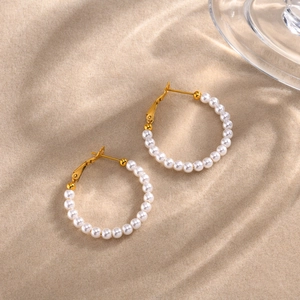 Detalle de pendientes de aro dorados con perlas blancas sobre un fondo de arena de playa