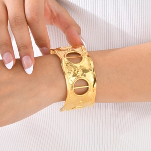 Macro detail of wide gold cuff bracelet featuring hammered texture and circular cutouts