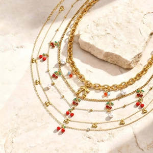 Détail de colliers dorés avec pendentifs cerise, perles et perles colorées sur fond pierre beige