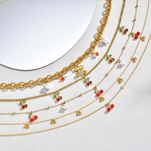 Collier cerise doré avec pendentifs en émail rouge, perles et nœuds sur fond blanc