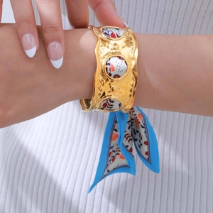 Macro shot of wide gold hammered cuff bracelet with floral silk scarf wrap detail