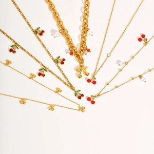 Vue à plat de plusieurs colliers et bracelets cerise dorés avec détails en perles