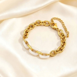 Detailed view of golden link chain bracelet with white resin accents on silk fabric