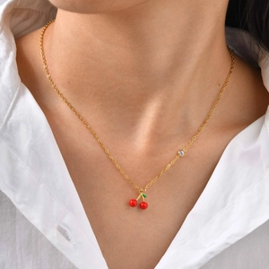 Détail du collier cerise doré avec pendentifs en émail rouge et zircon sur une chemise blanche