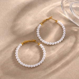 Detalle de pendientes de aro dorados con perlas blancas brillantes sobre fondo de arena
