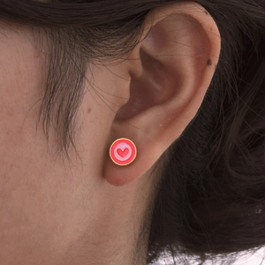 Vue détaillée des boucles d'oreilles cœur en émail portées sur l'oreille