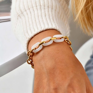 Close-up of gold chain bracelet with three white oval links on a sweater sleeve