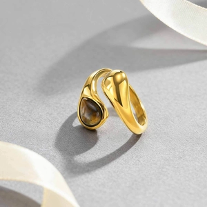 Detailed close-up of golden teardrop ring with brown tiger eye stone on grey surface