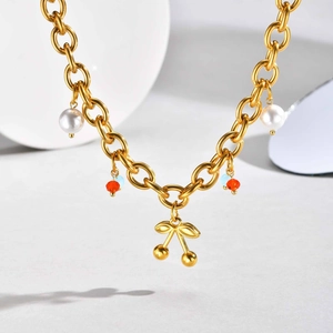 Détail macro du collier chaîne dorée avec pendentif cerise, perles et billes cristal