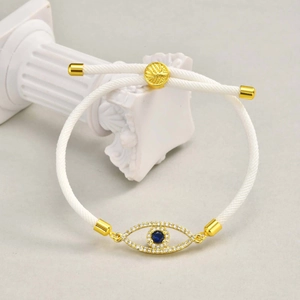 Close-up of evil eye charm with blue gemstone on white adjustable woven bracelet