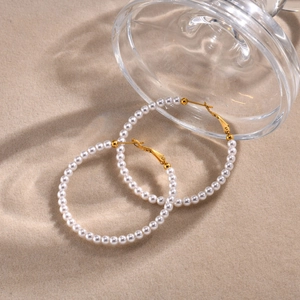 Detalle de pendientes de aro dorados con perlas blancas sobre fondo beige texturizado