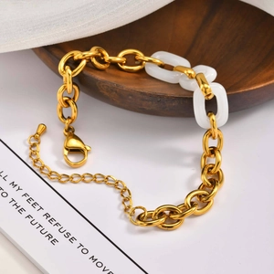 Gold stainless steel link chain bracelet with white ring accents on a wooden tray