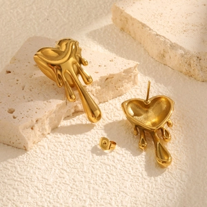 Gros plan de boucles d'oreilles cœur liquide fondu dorées sur une pierre texturée blanche