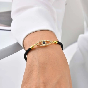 Close-up of golden Evil Eye charm on black woven cord bracelet with sparkling blue stone
