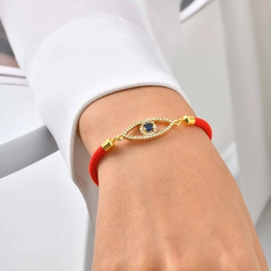 Close-up of golden Evil Eye charm with blue stone on red braided rope bracelet