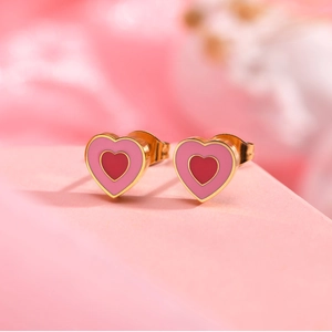 Détail macro de boucles d'oreilles cœur en or avec émail rose sur un support de vente
