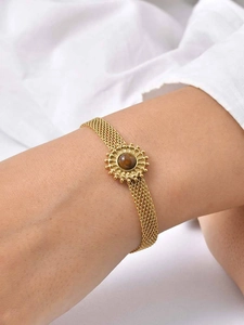 Détail d'un bracelet en maille dorée orné d'une pierre œil de tigre sur un poignet