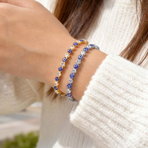 Icy gold and silver evil eye tennis bracelets with blue stones on a model's wrist