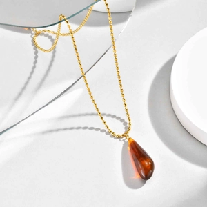 Detailed macro view of golden ball chain and translucent amber teardrop pendant necklace