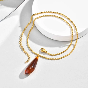 Macro view of golden bead chain necklace with amber resin teardrop pendant detail
