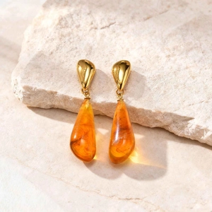 Vintage gold water drop earrings with amber resin teardrops on natural stone background