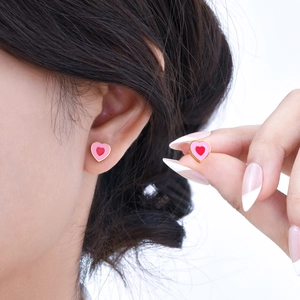 Boucles d'oreilles cœur rose et rouge avec bordure dorée portées et tenues à la main
