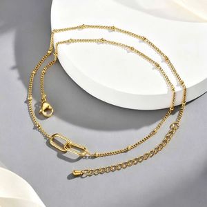 Detail of gold layered necklace with metallic beads and intertwined double rings on a white base