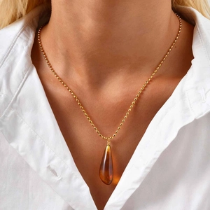 Detail of amber resin teardrop pendant on gold bead chain necklace worn by model