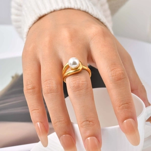 Close-up of elegant gold ring with 8mm white pearl worn on index finger holding a cup