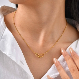 Close-up of minimalist gold beaded chain with interlocking double oval rings on neck