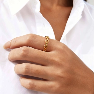 Detailed view of a golden chain-link ring worn against a soft white shirt background