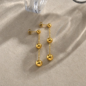 Detail of golden stainless steel drop earrings with layered ball tassel design and shadow