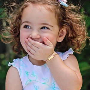 Girl wearing a gold-tone ID bracelet with a pink flower charm on a thin chain