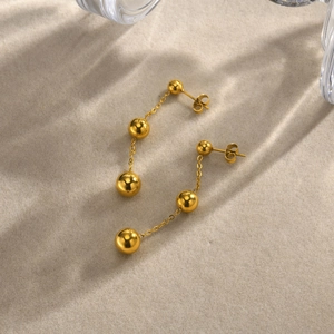 Macro detail of gold-plated stainless steel ball drop earrings with elegant draping chains
