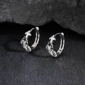 Detail of gothic stainless steel hoop earrings with rose, cross and zircon on dark rock