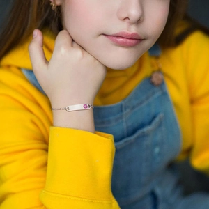 Detail of custom silver child ID bracelet with a pink flower charm on a model's wrist