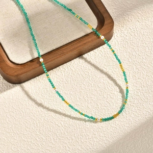 Dettaglio di una collana bohémien con perline di vetro verde sfaccettato e perle bianche
