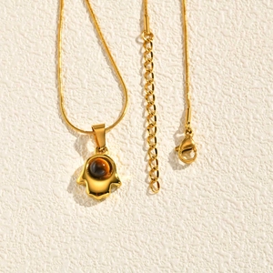 Dettaglio del ciondolo Mano di Fatima dorato con occhio di tigre su catena snake