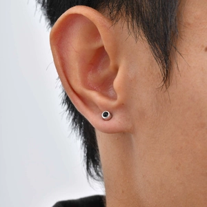 Macro shot of a silver metal ear clip with a round black zircon stone worn on the earlobe